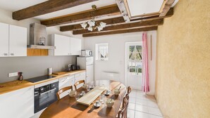 Una cucina con travi in legno, mobili bianchi, un tavolo da pranzo con sedie e vista all'esterno tramite una porta.
