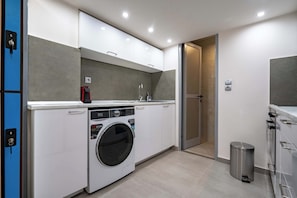 A compact laundry room with a front-loading washing machine, a small sink, and a trash can.