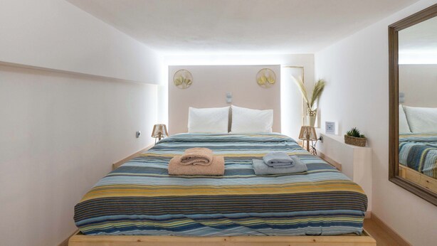A bedroom with a bed, two pillows, a bedside table with a lamp, and a mirror on the wall. - Loft 53 – Twin Loft II by ΜΡS (Athens)