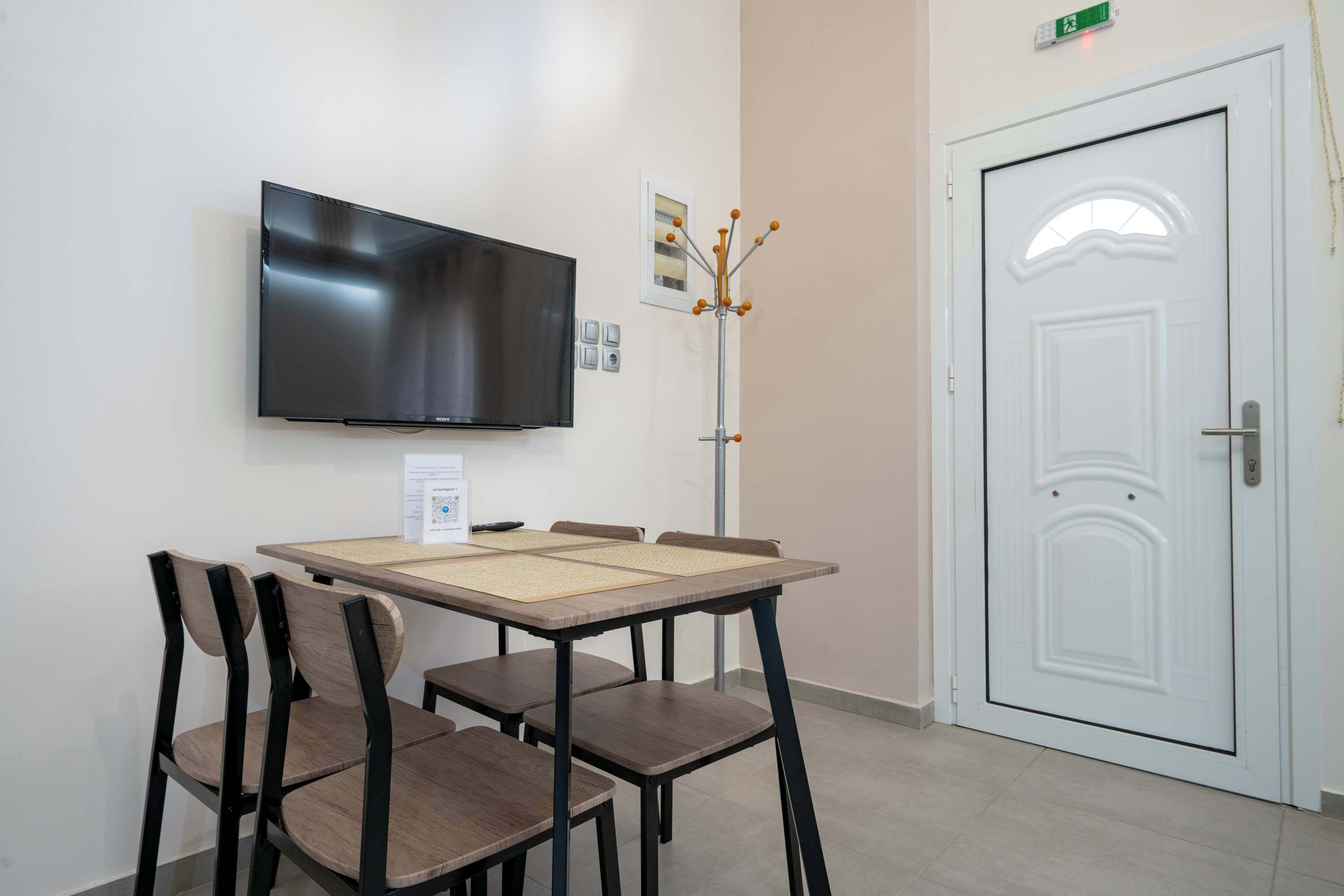 A room with a flat-screen TV mounted on the wall, a white door, and a table with chairs.