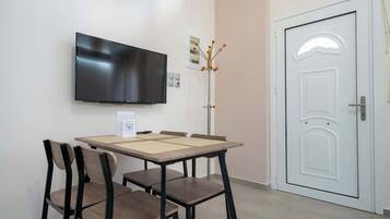 A room with a flat-screen TV mounted on the wall, a white door, and a table with chairs.