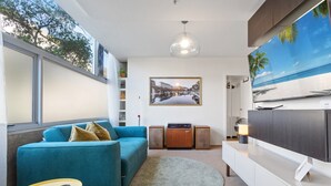 Un salon moderne avec un canapé de couleur turquoise, un grand téléviseur à écran plat, un meuble en bois et un tableau encadré accroché au mur.