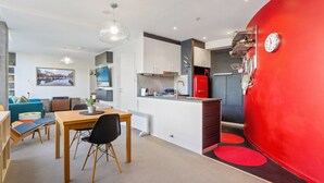 Une cuisine moderne avec des meubles blancs, un réfrigérateur rouge et un coin repas comprenant une table et des chaises en bois.