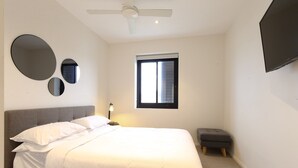 A bedroom with a bed, a ceiling fan, a window, a TV, and three wall-mounted mirrors. - Comfy 2-Bedroom Apartment with a Clyde River View (North Batemans Bay)