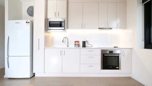 A modern kitchen with white cabinetry, a built-in microwave, a refrigerator, and an oven. - Comfy 2-Bedroom Apartment with a Clyde River View (North Batemans Bay)