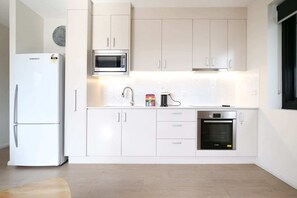 A modern kitchen with white cabinetry, a built-in microwave, a refrigerator, and an oven. - Comfy 2-Bedroom Apartment with a Clyde River View (North Batemans Bay)