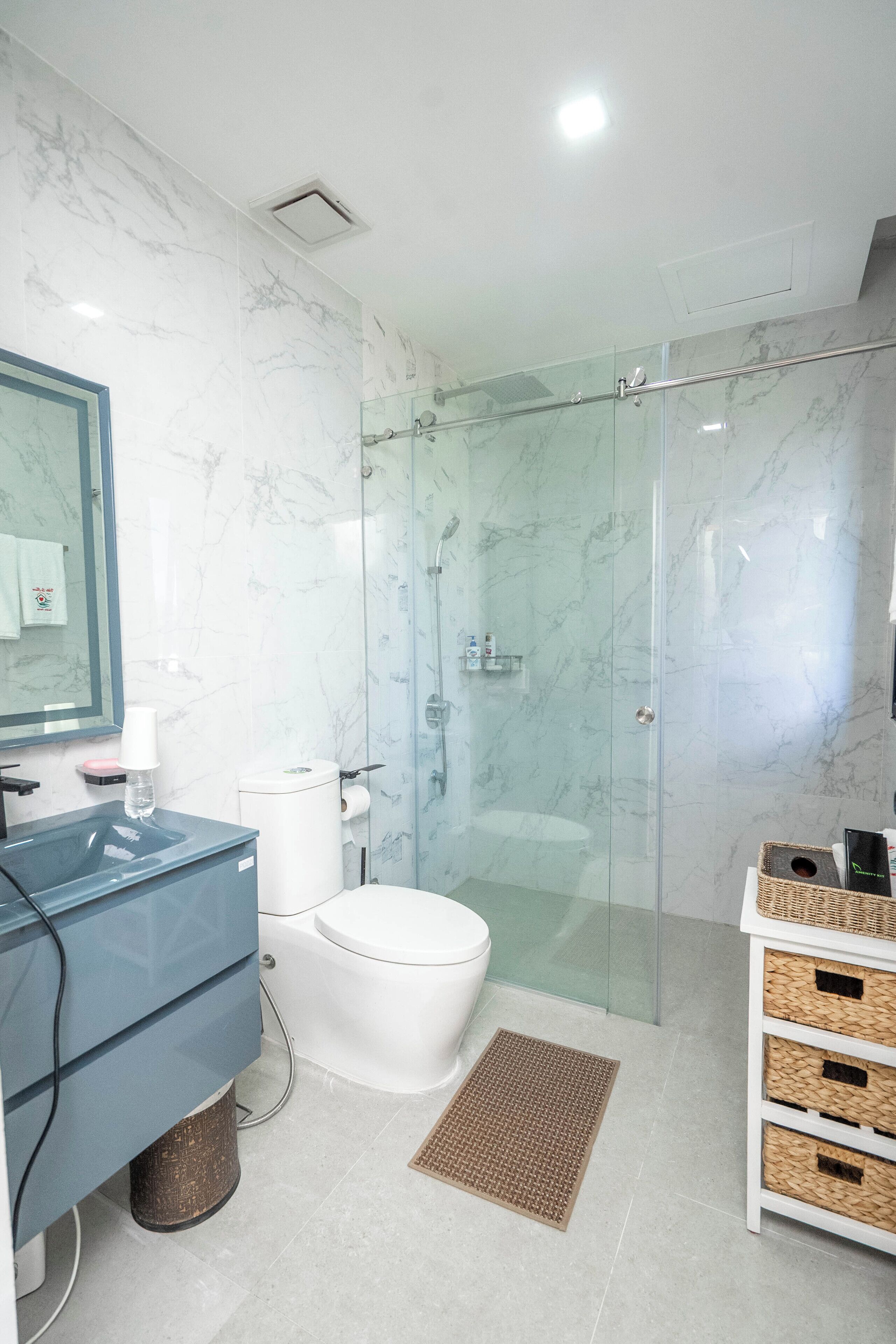 Een moderne badkamer met een douchecabine van glas, een wit toilet, een blauwe wastafel en een spiegel met een handdoek erop.