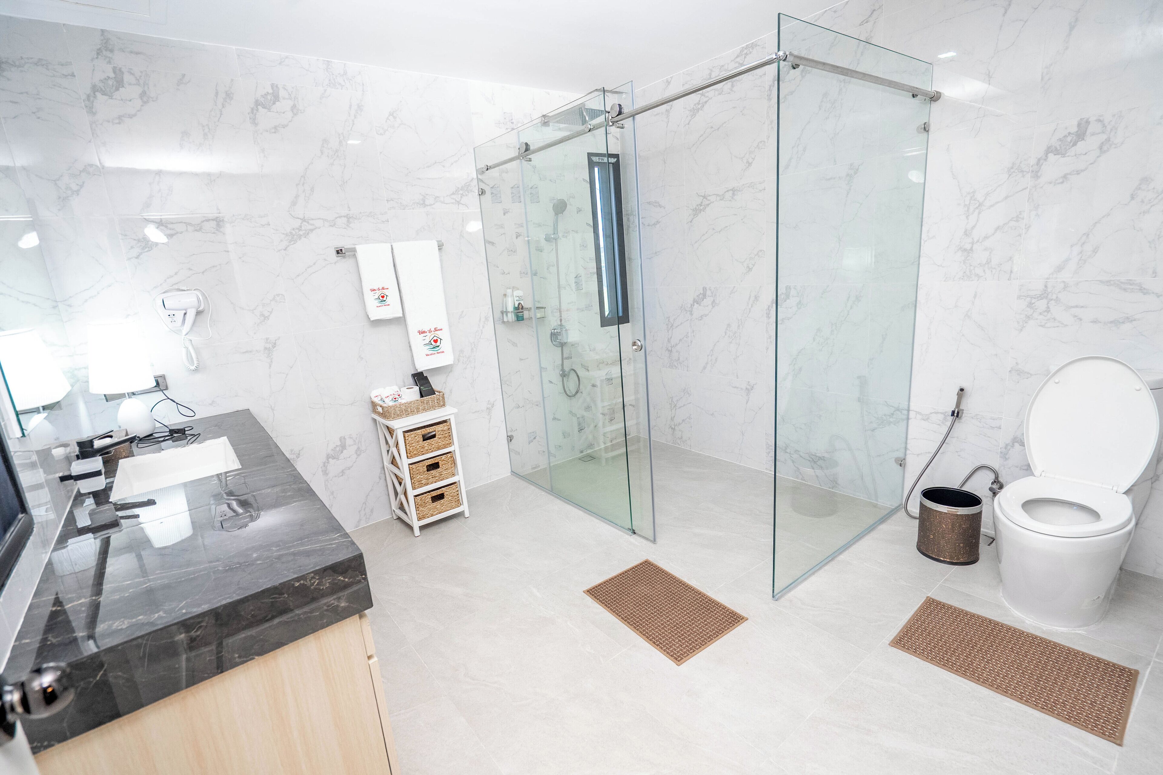 Un baño moderno con ducha envuelta en vidrio, inodoro y tocador con lavamanos.