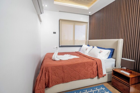 A hotel room with a bed, a nightstand, a lamp, and a window with blinds.