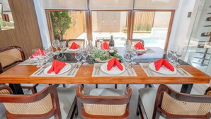 Une table à manger dressée avec des serviettes rouges, des assiettes blanches et des verres transparents, donnant sur une piscine grâce à de grandes fenêtres.
