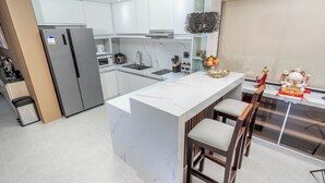 Une cuisine moderne avec des meubles blancs, un îlot en marbre et un coin bar avec des tabourets.