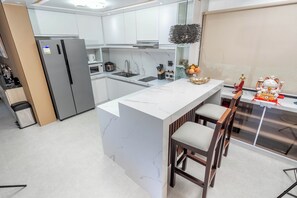 Una cocina moderna con armarios blancos, una isla de mármol y una zona de bar con taburetes.