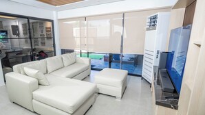 Una sala de estar moderna con un sofá seccional, un reposapiés pequeño y un televisor de pantalla plana.