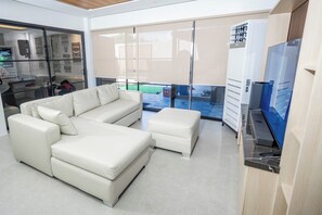 Una sala de estar moderna con un sofá seccional, un reposapiés pequeño y un televisor de pantalla plana.