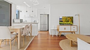 Une cuisine moderne avec des meubles blancs, un réfrigérateur en acier inoxydable et un coin repas comprenant une table et des chaises en bois.