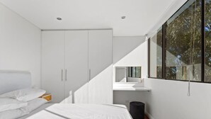 Une chambre moderne avec un lit, une armoire blanche et une grande fenêtre donnant sur un paysage arboré.