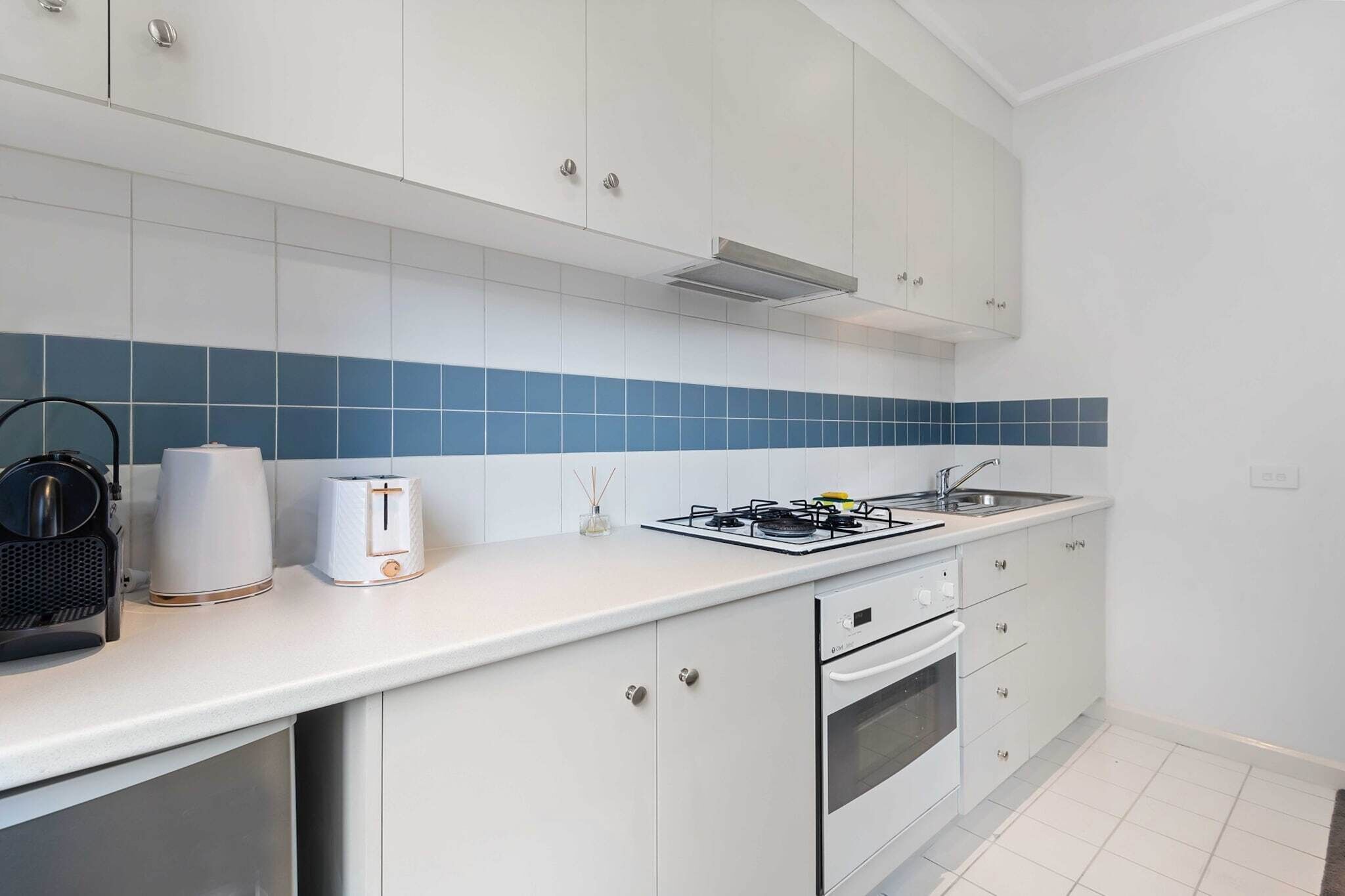 A modern kitchen with white cabinets, a gas stove, a sink, and a toaster.