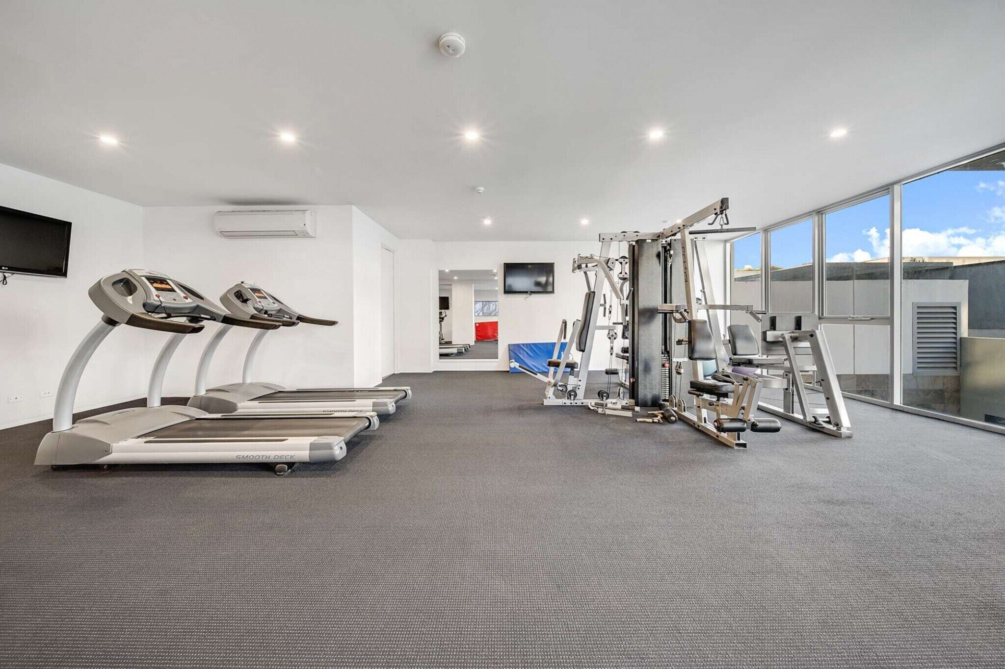 Un gimnasio con cintas de correr, máquinas de pesas y una pantalla de televisión.