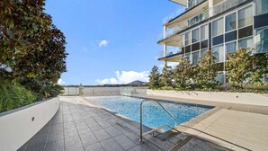 A modern outdoor swimming pool with a clear view of the sea and a building with balconies. - Canberra Lakefront 2-Bed with Pool, (Kingston)
