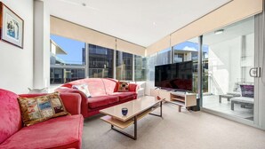 A modern living room with a red sofa, a coffee table, and a TV. - Canberra Lakefront 2-Bed with Pool, (Kingston)