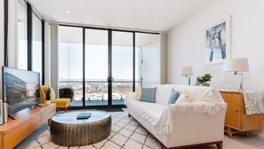 Ein modernes Wohnzimmer mit großem Fenster, einem weißen Sofa, einem Holztisch und einem Fernseher auf einer Holzkonsole.