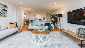 Een moderne woonkamer met een witte bank, een houten salontafel en een grote televisie die aan de muur is bevestigd.