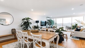 Een ruime woonkamer met een houten eettafel, witte stoelen en een groot raam met uitzicht.