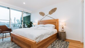 Een moderne slaapkamer met een houten bed, uitzicht op groen en een klein nachtkastje met een lamp.
