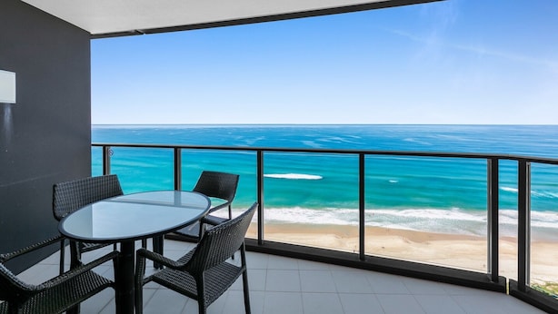 En balkon med et glastæppe og stole, med udsigt over en strand og hav.