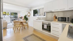 A modern kitchen with white cabinets, a microwave, and a stove. There is a dining area with a table and chairs. - Ground Floor 2-Bed Mermaid Beach Pad with Parking (Mermaid Beach)
