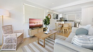 A modern living room with a sofa, a wooden coffee table, a wicker chair, a TV, and a dining area with chairs and a table. - Ground Floor 2-Bed Mermaid Beach Pad with Parking (Mermaid Beach)