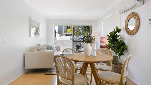 A modern living room with a round wooden dining table, wicker chairs, a white sofa, and a large potted plant. - Ground Floor 2-Bed Mermaid Beach Pad with Parking (Mermaid Beach)