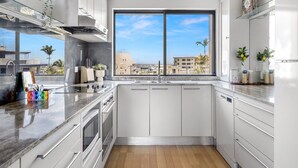 Een moderne keuken met witte kastjes, een groot raam en uitzicht op de stad.