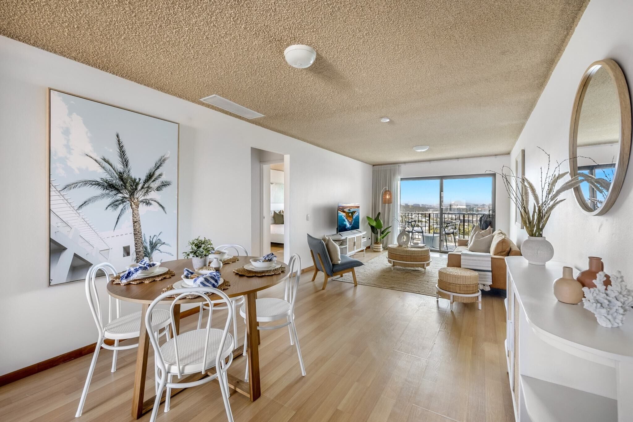 Een ruime woonkamer met een eettafel, witte stoelen, een bank en een groot raam met uitzicht op de stad.