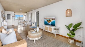 Een moderne woonkamer met een grote televisie, een eethoek en een keuken op de achtergrond.