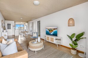 Ein modernes Wohnzimmer mit großem Fernseher, Essbereich und einer Küche im Hintergrund.