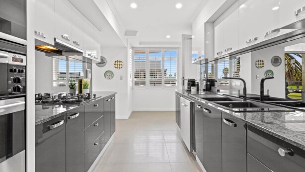 Una cocina moderna con electrodomésticos de acero inoxidable, armarios grises y un ventanal que ofrece luz natural.