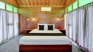 Een slaapkamer met houten lambrisering, een groot bed, twee nachtkastjes en een airconditioning unit aan het plafond.