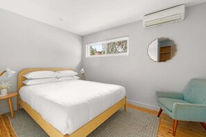 Un dormitorio con cama, una silla, una mesita de noche, una ventana y un equipo de aire acondicionado.