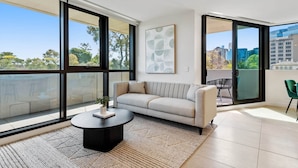 Un salon moderne avec un canapé, une table basse et une vue sur la ville grâce à de grandes fenêtres.