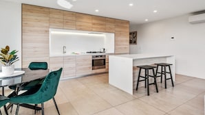 Une cuisine moderne dotée d’un îlot central, de meubles en bois et d’un coin repas avec une table ronde et des chaises de couleur turquoise.