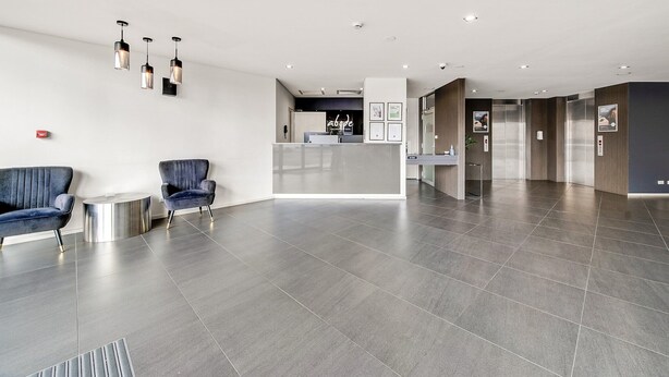 A modern lobby with a reception desk, two blue armchairs, and a small round table.