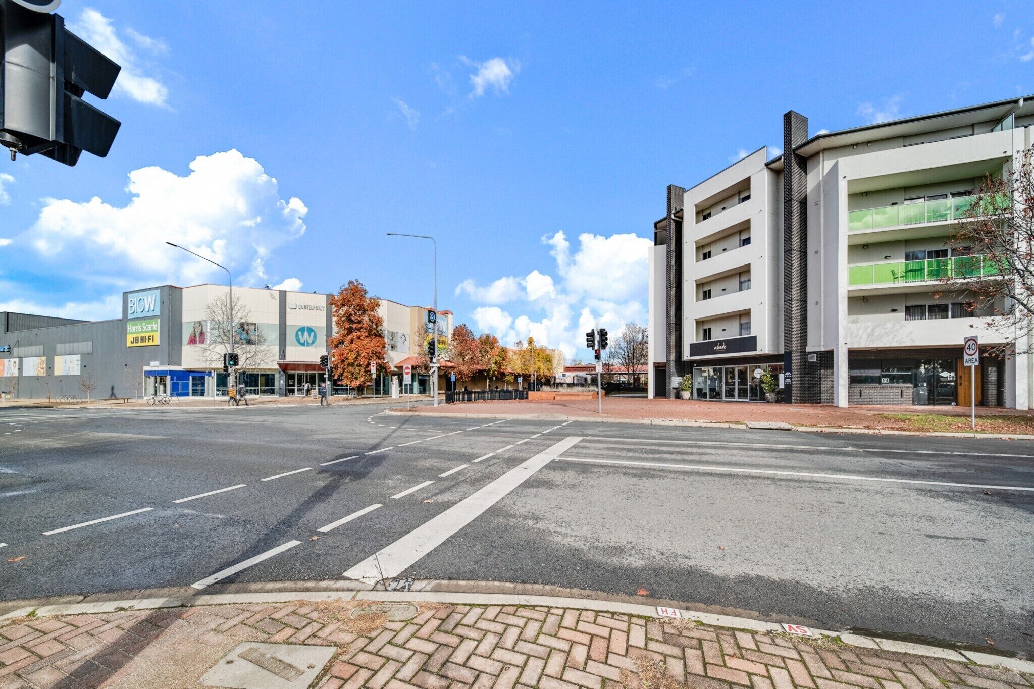 A street intersection with a modern building featuring a large sign for BICW, a commercial area with autumn-colored trees, and a clear blue sky.