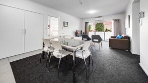 A modern living room with a dining area, white furniture, and a large window with curtains.