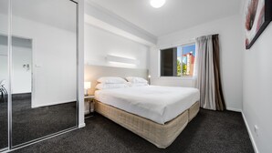A modern hotel room with a large bed, a bedside table, a mirror, and a window with curtains.