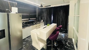 A modern kitchen with a white countertop, black marble flooring, and a purple chair. - THE PAD BY FRACSPACE (Hyderabad)