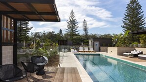 Un espace piscine extérieur moderne, doté de chaises longues, d’une terrasse en bois et offrant une vue sur les arbres environnants.