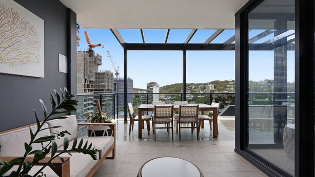 Un balcon moderne doté d’une paroi vitrée, un coin repas avec une table et des chaises, et un canapé.
