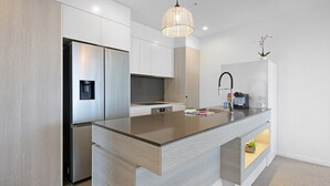 Une cuisine moderne dotée d’un îlot central, d’appareils électroménagers intégrés et d’un luminaire suspendu.