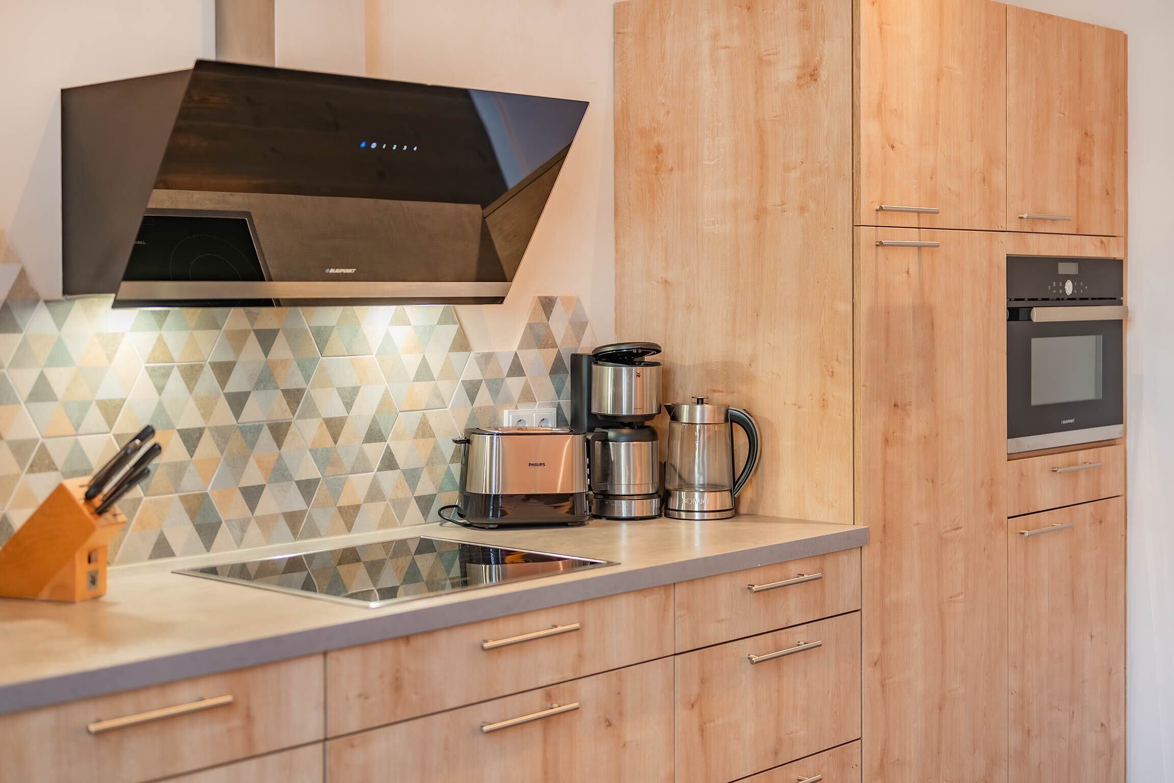 Une cuisine moderne équipée d’une cuisinière intégrée, d’une machine à café et d’un grille-pain posés sur le plan de travail.